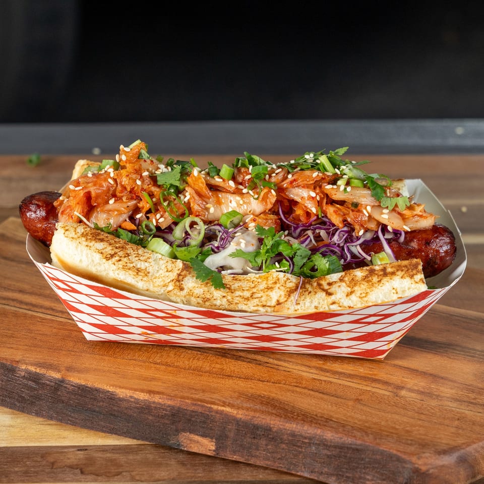 Tako Cheena's Asian-fusion hot dog with kimchi, cabbage, and cilantro in a paper tray.