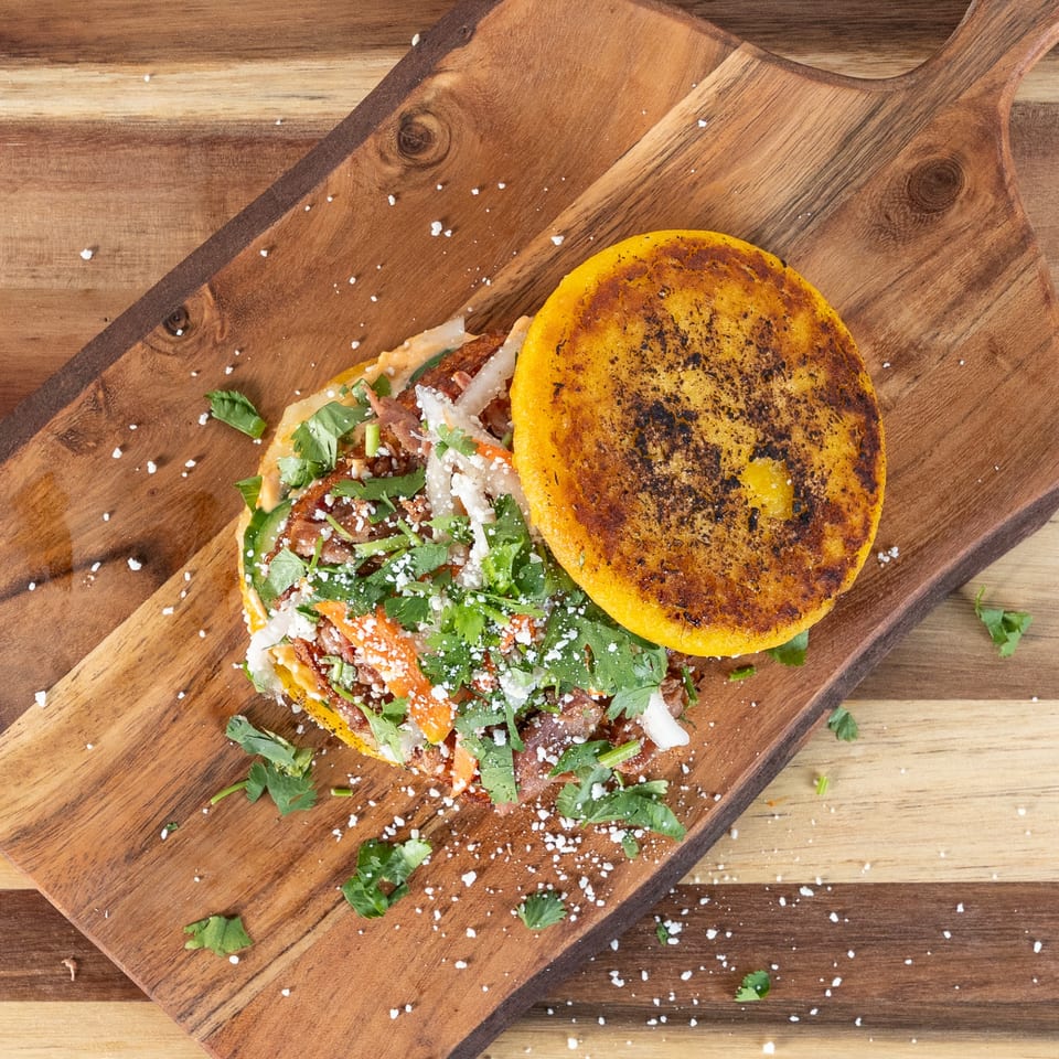 Tako Cheena's Asian-fusion arepa with meat, cilantro, and cheese on a wooden board.