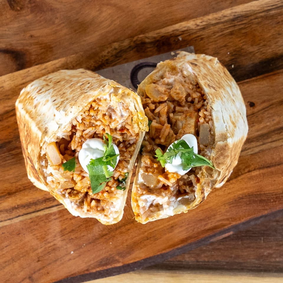 Two halves of a Tako Cheena burrito, filled with rice and meat, topped with sour cream and cilantro.