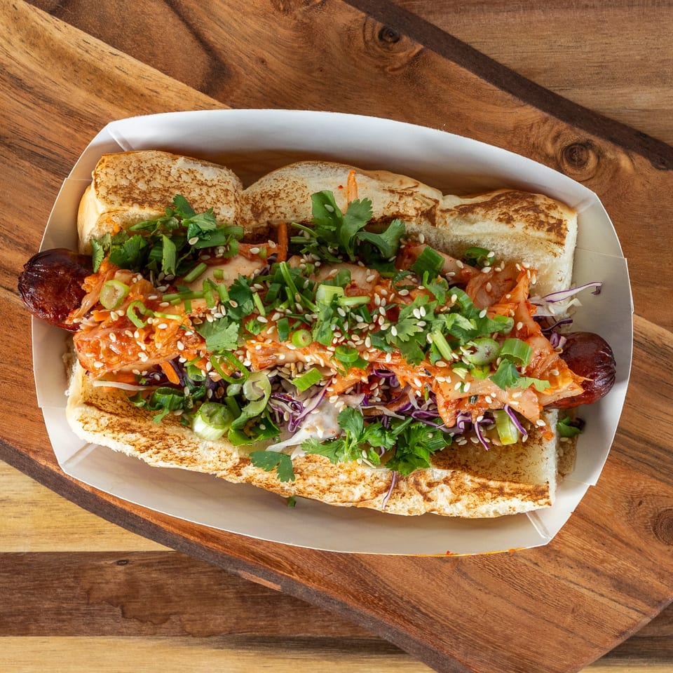 Tako Cheena's Asian-fusion hot dog with kimchi, cilantro, sesame seeds, and scallions in a toasted bun.