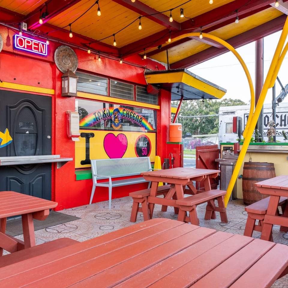 Tako Cheena's vibrant red and yellow exterior with outdoor picnic tables and an "OPEN" sign.