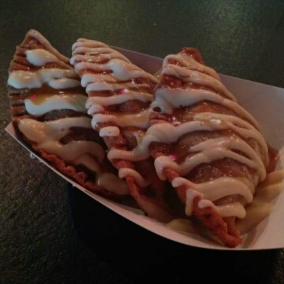 Three crispy dessert empanadas drizzled with white icing and caramel in a paper tray.