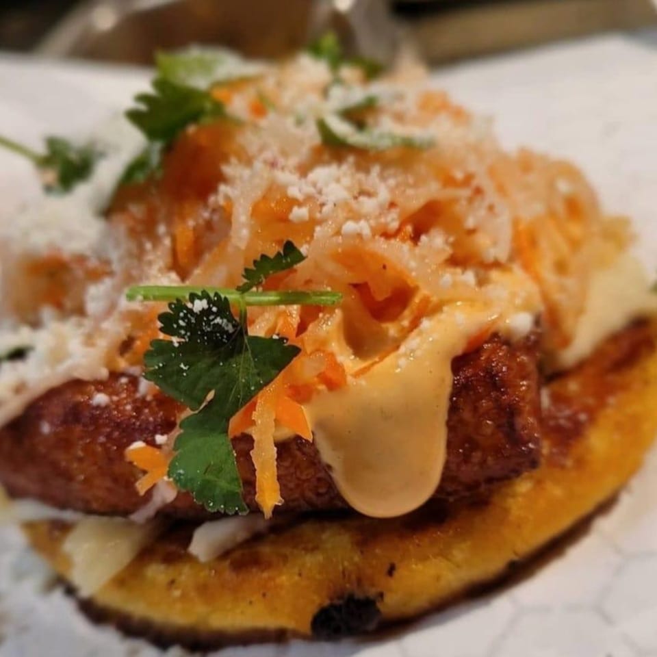 Close-up of a Tako Cheena Asian-fusion taco with fried chicken, sauce, shredded vegetables, and cilantro.